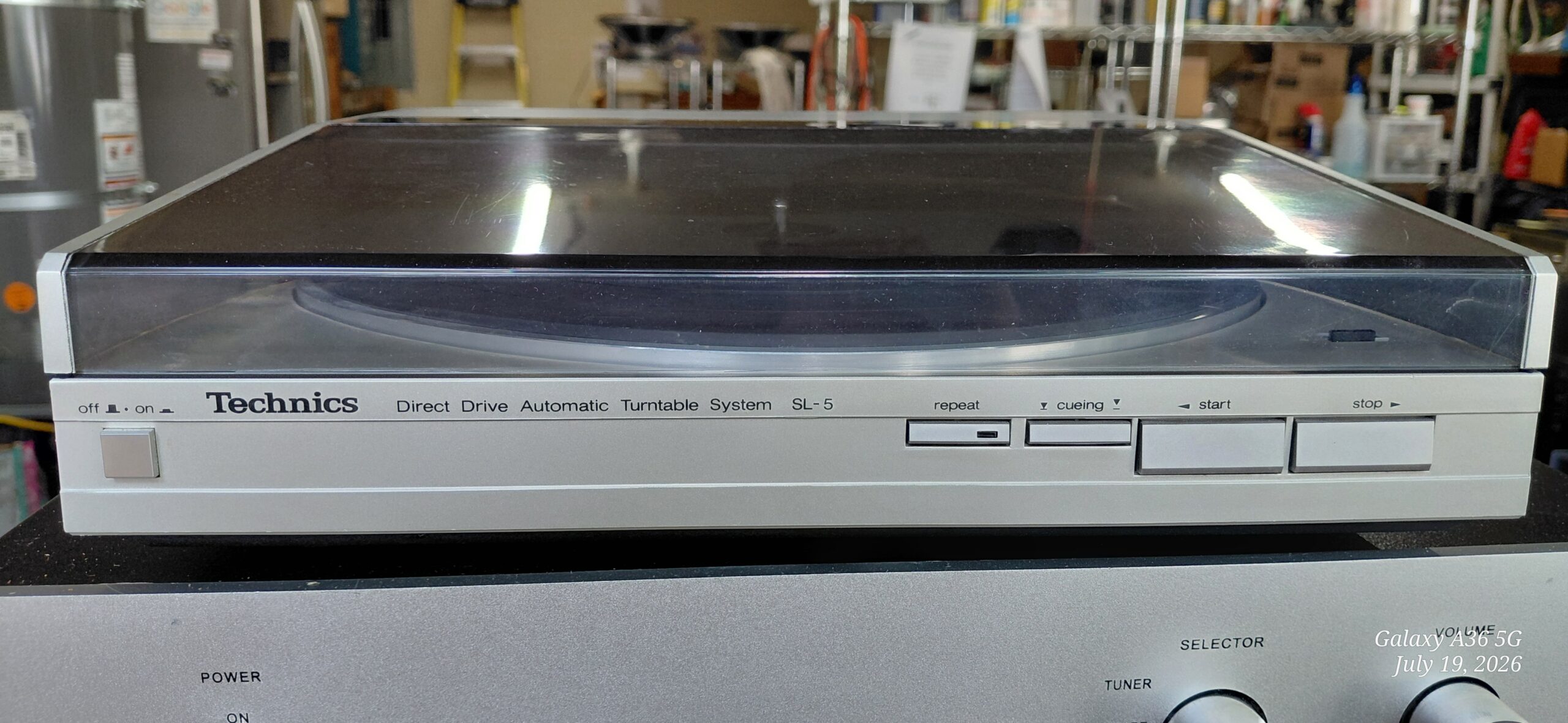 Technics SL-5 direct drive automatic turntable with dust cover closed, sitting atop a stereo receiver